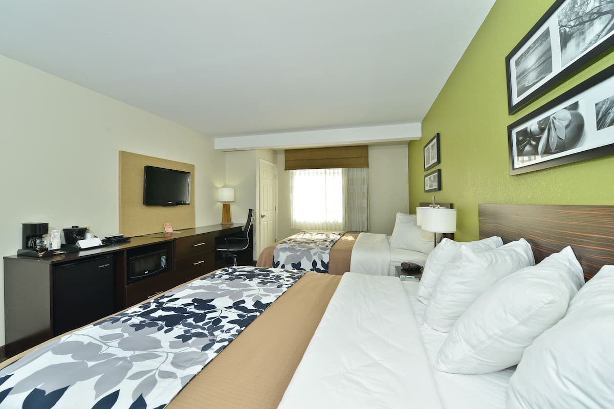 Habitación de hotel con dos camas, un escritorio con televisor y una zona de comedor.