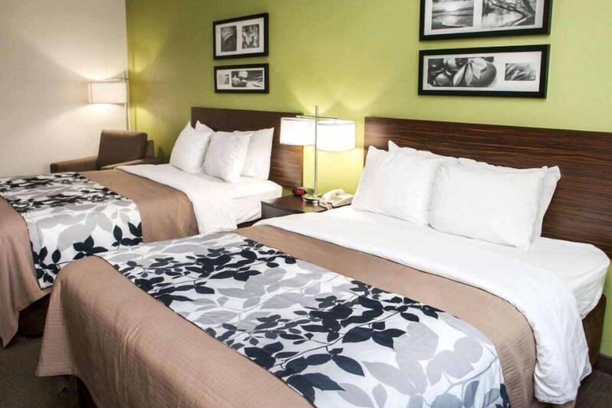 Una habitación de hotel con dos camas, una mesita de noche con lámpara y cuadros en la pared.
