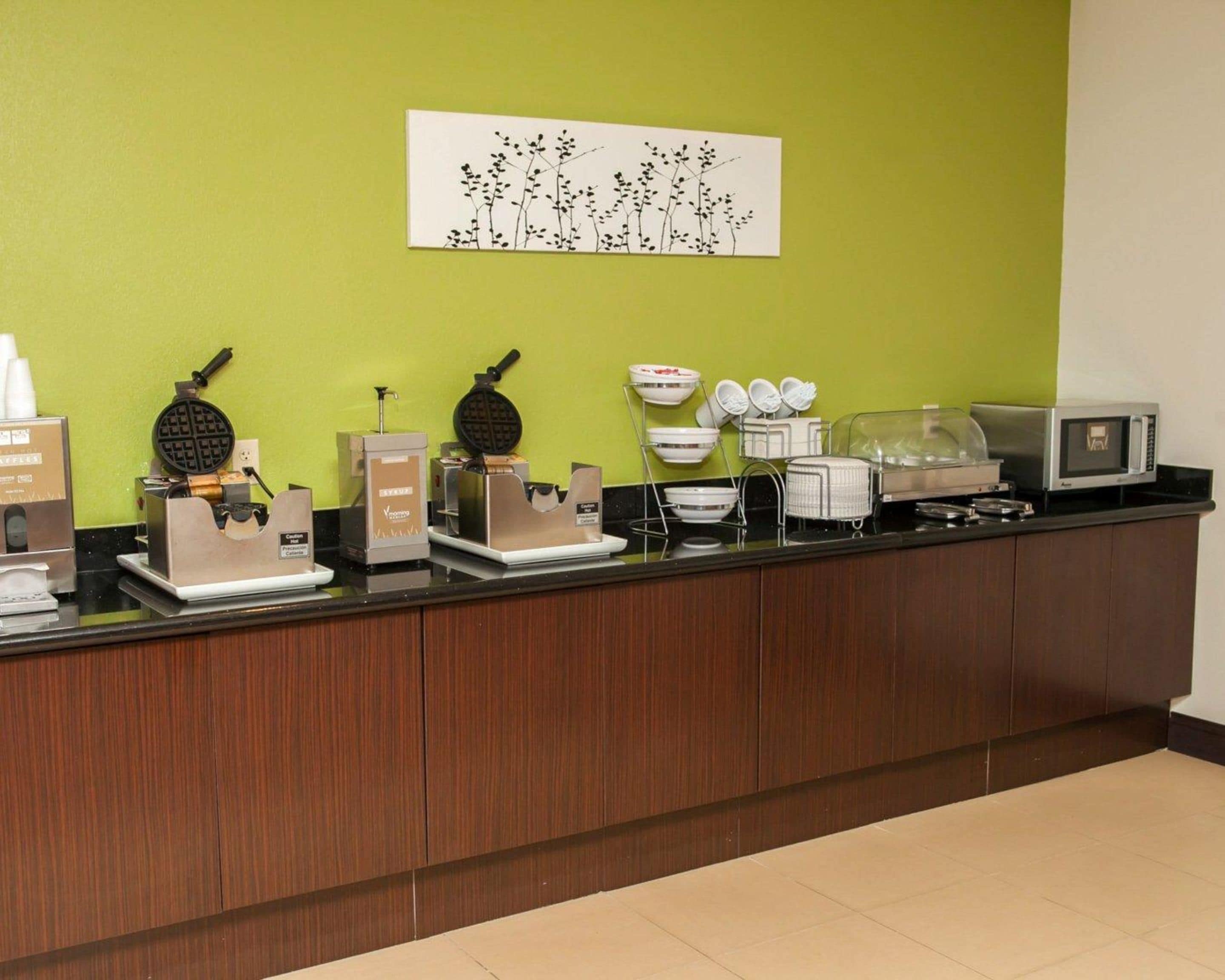 A breakfast bar with waffle makers, coffee machines, and a microwave.