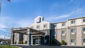 Un hotel de varios pisos con una entrada central, un asta con la bandera estadounidense y un cielo azul despejado.