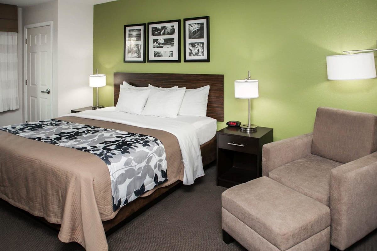 Habitación de hotel con cama, dos mesitas de noche, una silla y un cuadro en la pared.