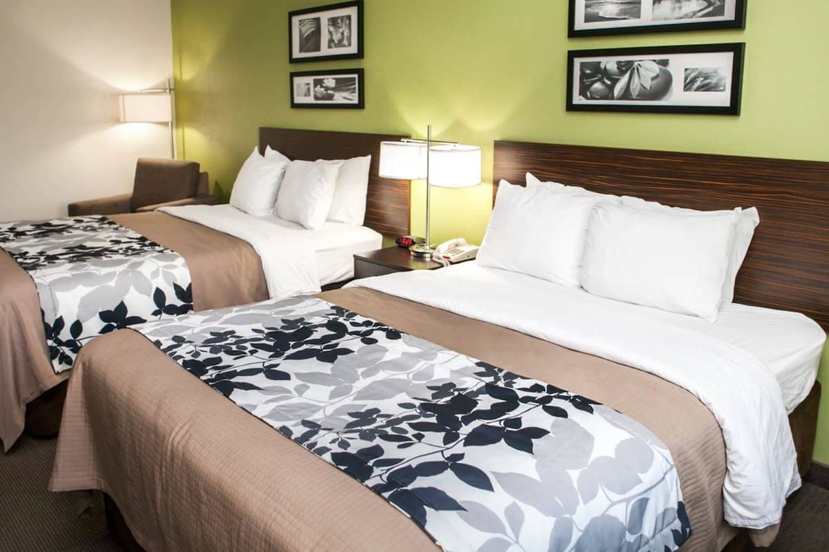 Una habitación de hotel con dos camas, una mesita de noche con lámpara y cuadros en la pared.