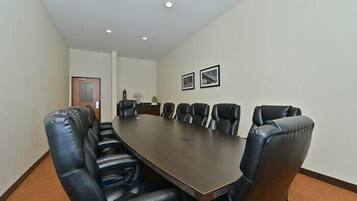 A conference room with a long table and black leather chairs, white walls, and framed pictures on the wall.