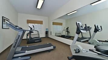 Un gimnasio con cintas de correr, una bicicleta estática y un espejo grande.