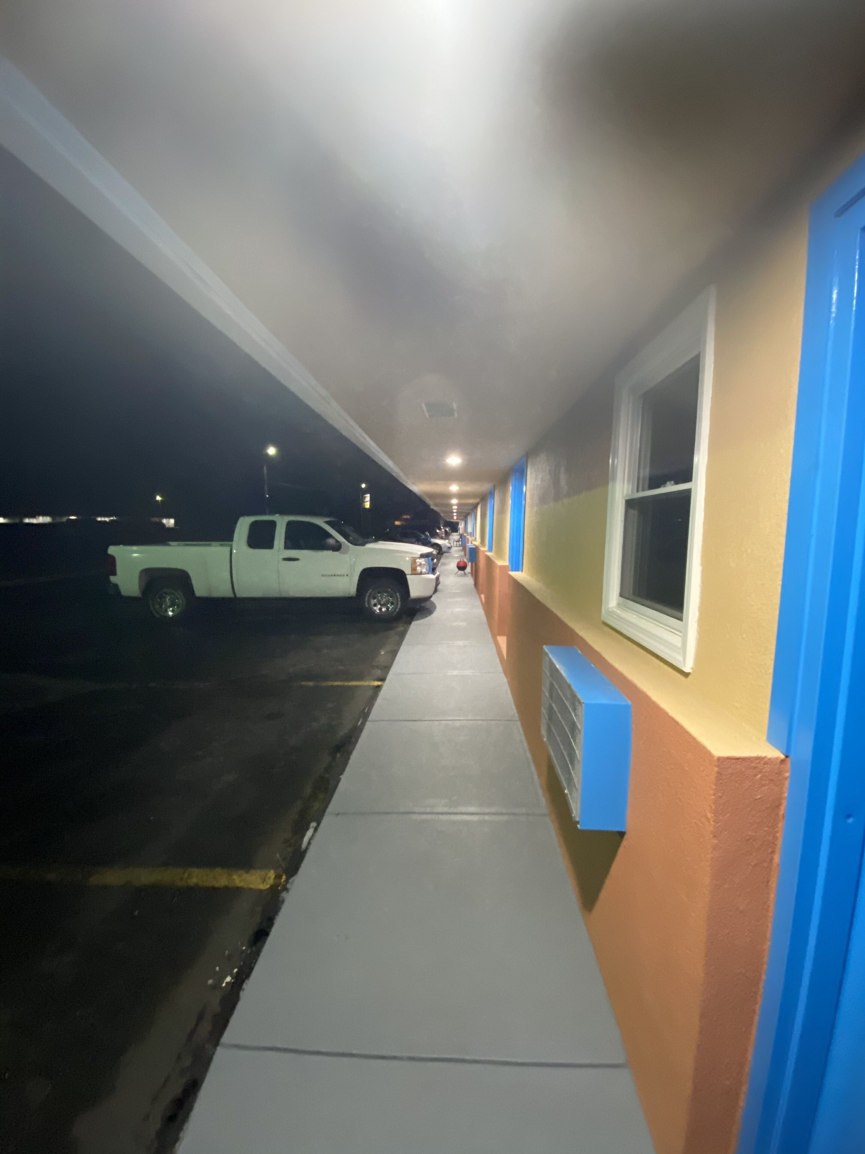 A hallway with a white truck parked on the left, a blue and beige wall with a window on the right, and a concrete floor.