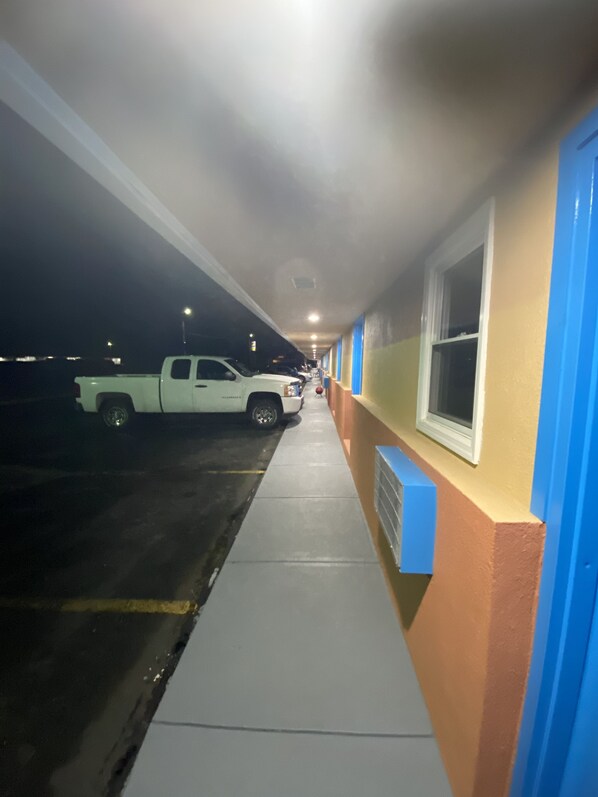 A hallway with a white truck parked on the left, a blue and beige wall with a window on the right, and a concrete floor. - Scottish Inns (Wrightstown)