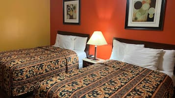 A hotel room with two beds, each with a patterned bedspread, a nightstand with a lamp, and two framed pictures on the walls.