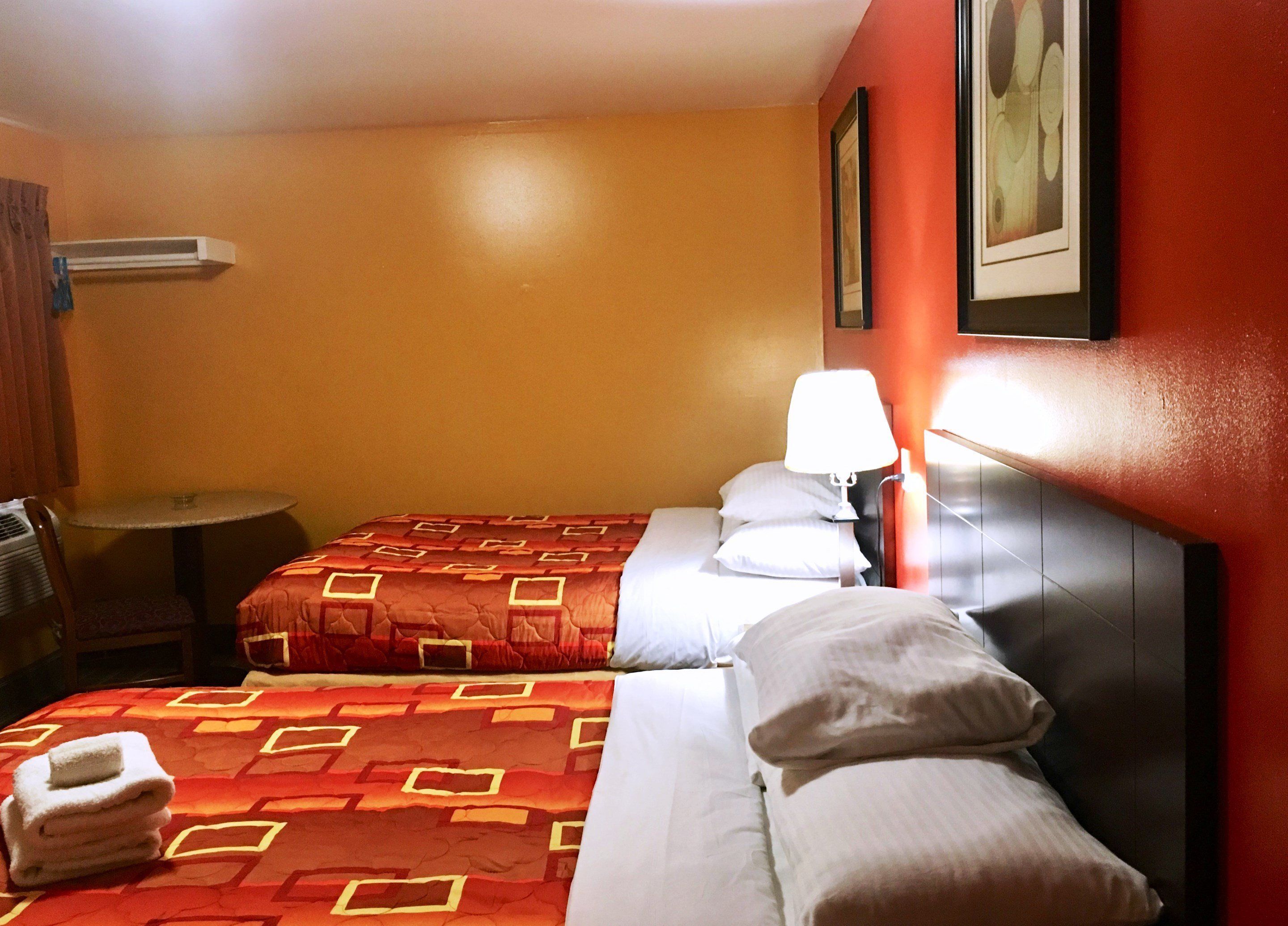 Quarto de hotel com cama, mesa de cabeceira, luminária, cadeira, ar condicionado fixado na parede e quadro emoldurado.