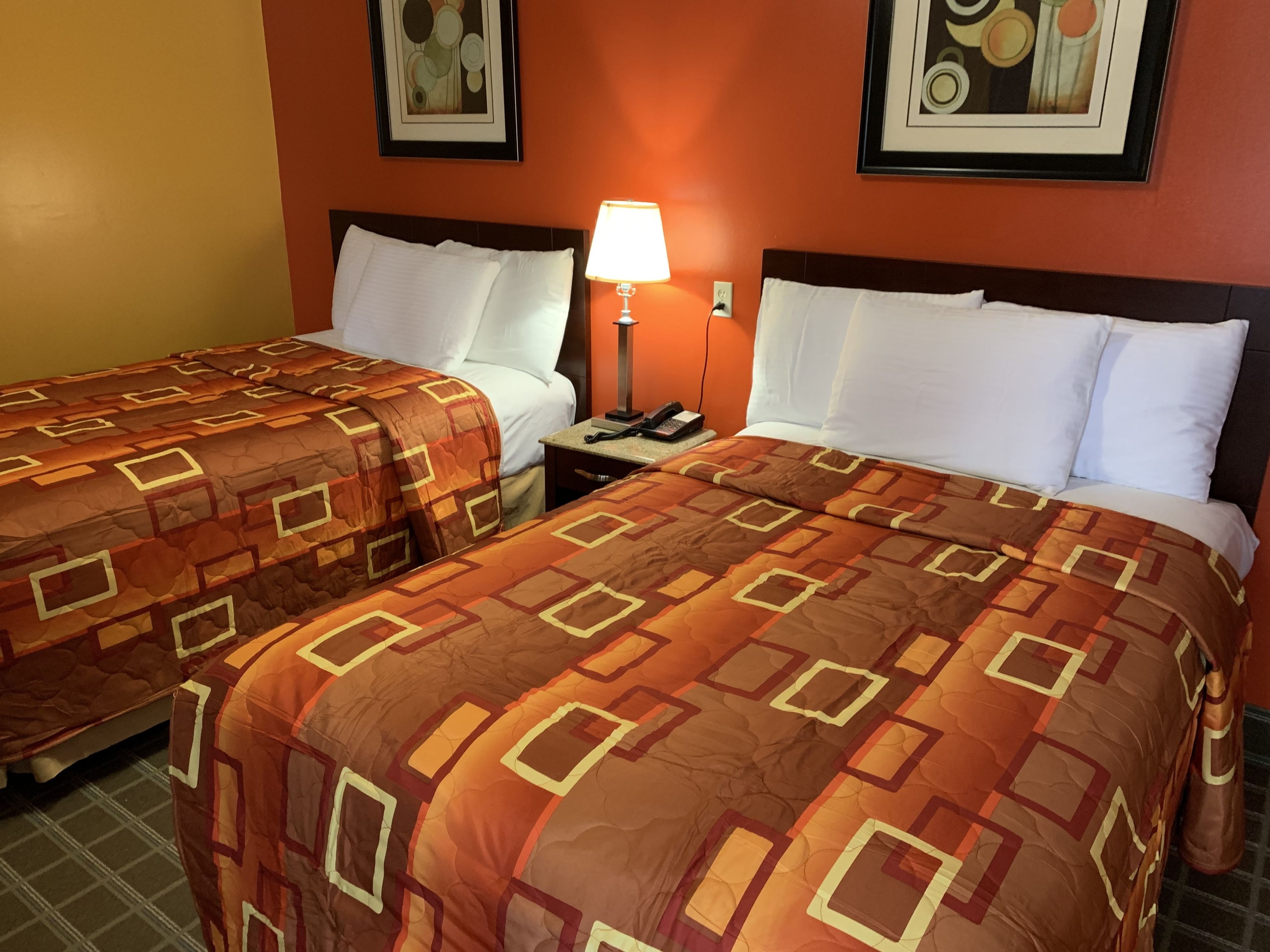 Habitación de hotel con dos camas, cada una con una colcha estampada, una lámpara de noche y una mesita de noche con teléfono.