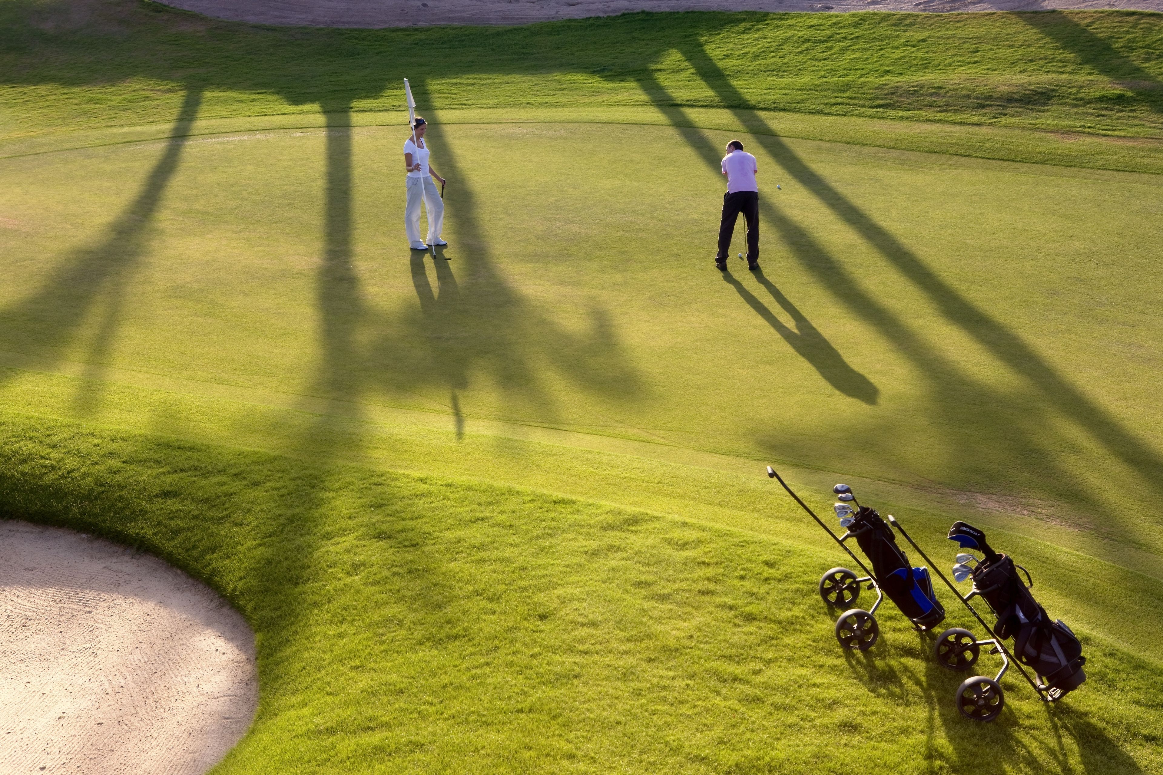 Een golfbaan met een putting green, zandbunkers en een golfkar.