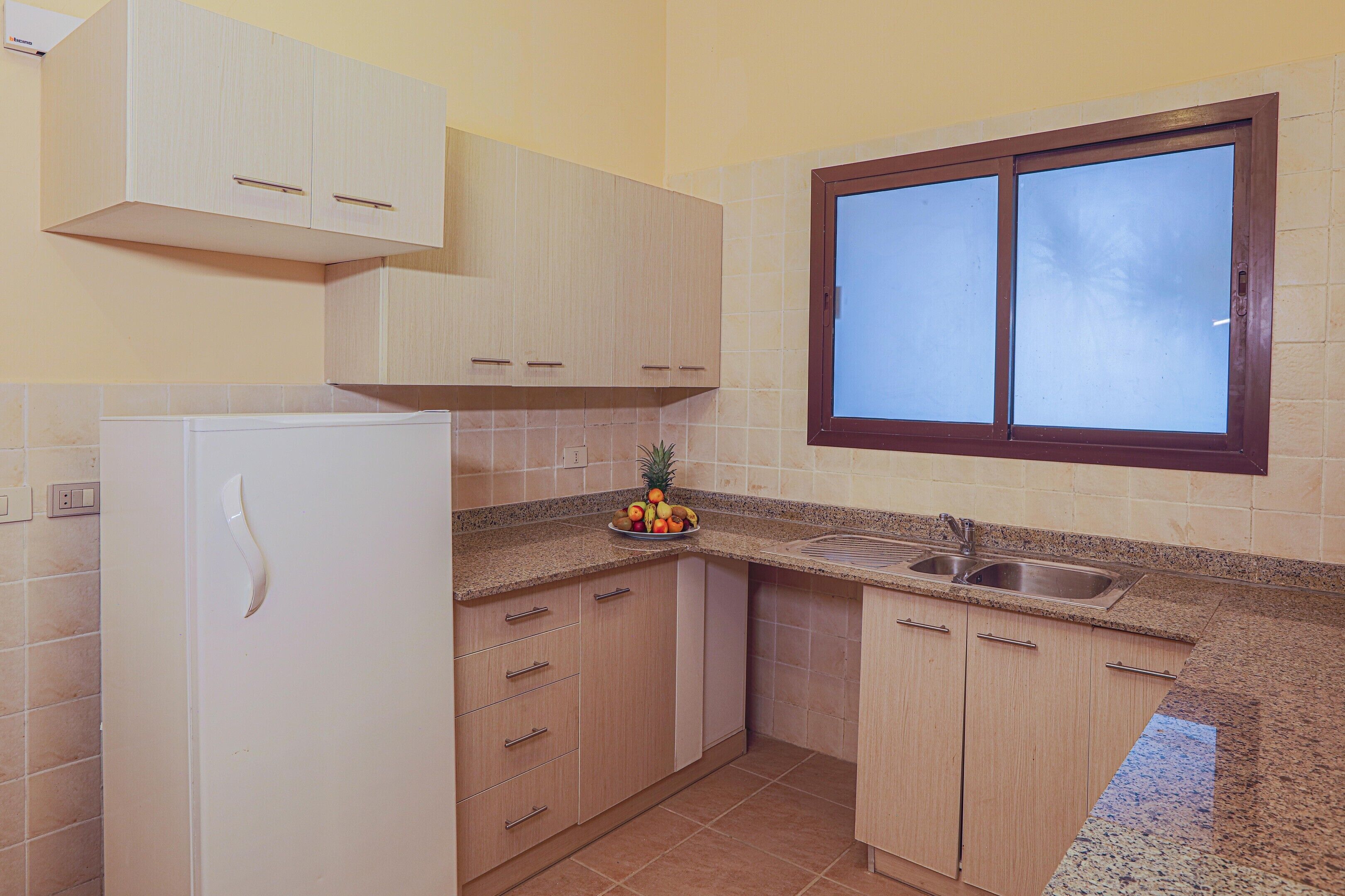 Una cocina con armarios de madera clara, un lavamanos de acero inoxidable y una ventana sobre el lavamanos.