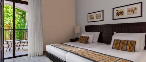 A hotel room with two beds, a balcony, and a view of greenery.