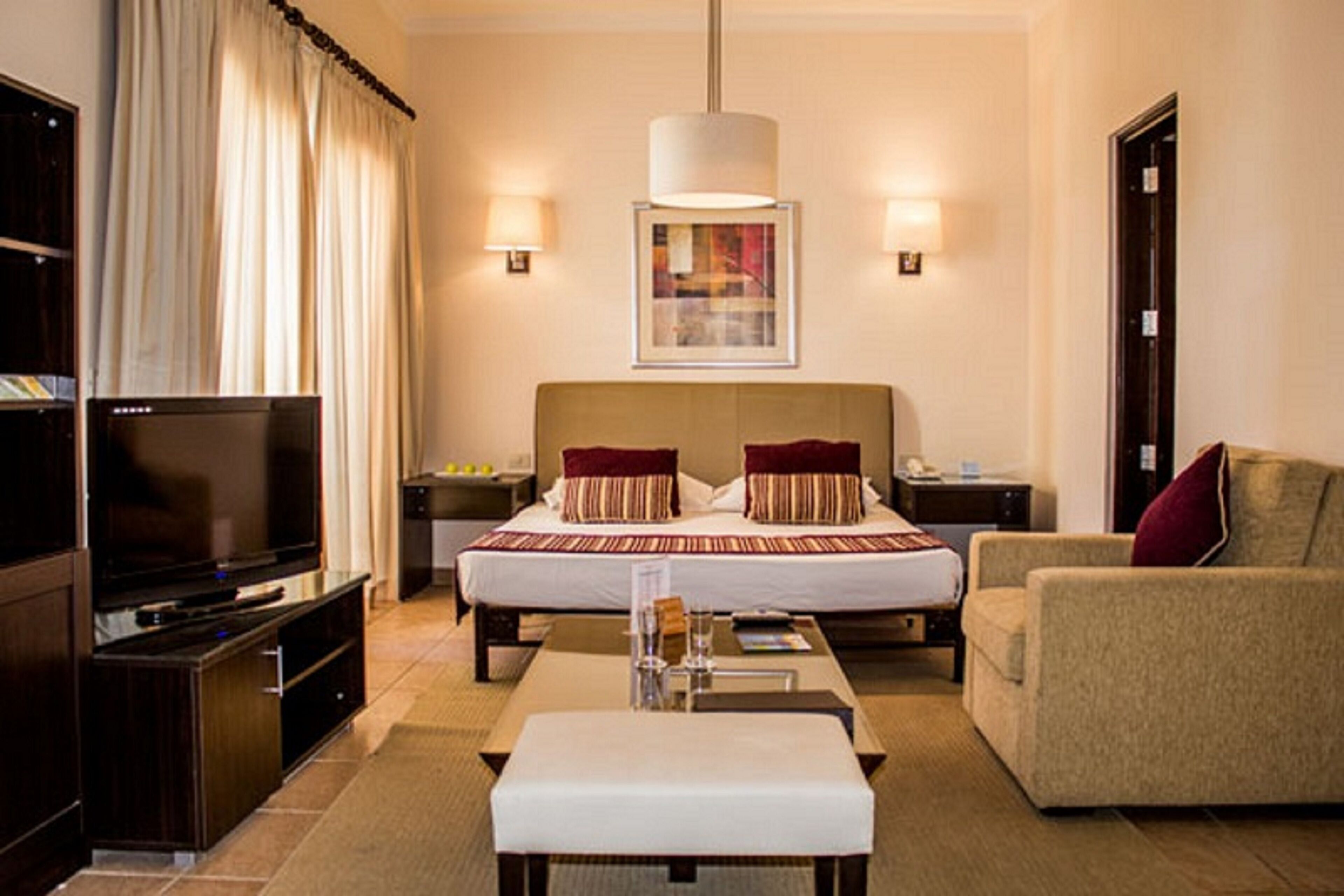 Una camera d'albergo con un letto grande, una televisione, un divano, un tavolino da caffè e un quadro appeso al muro.