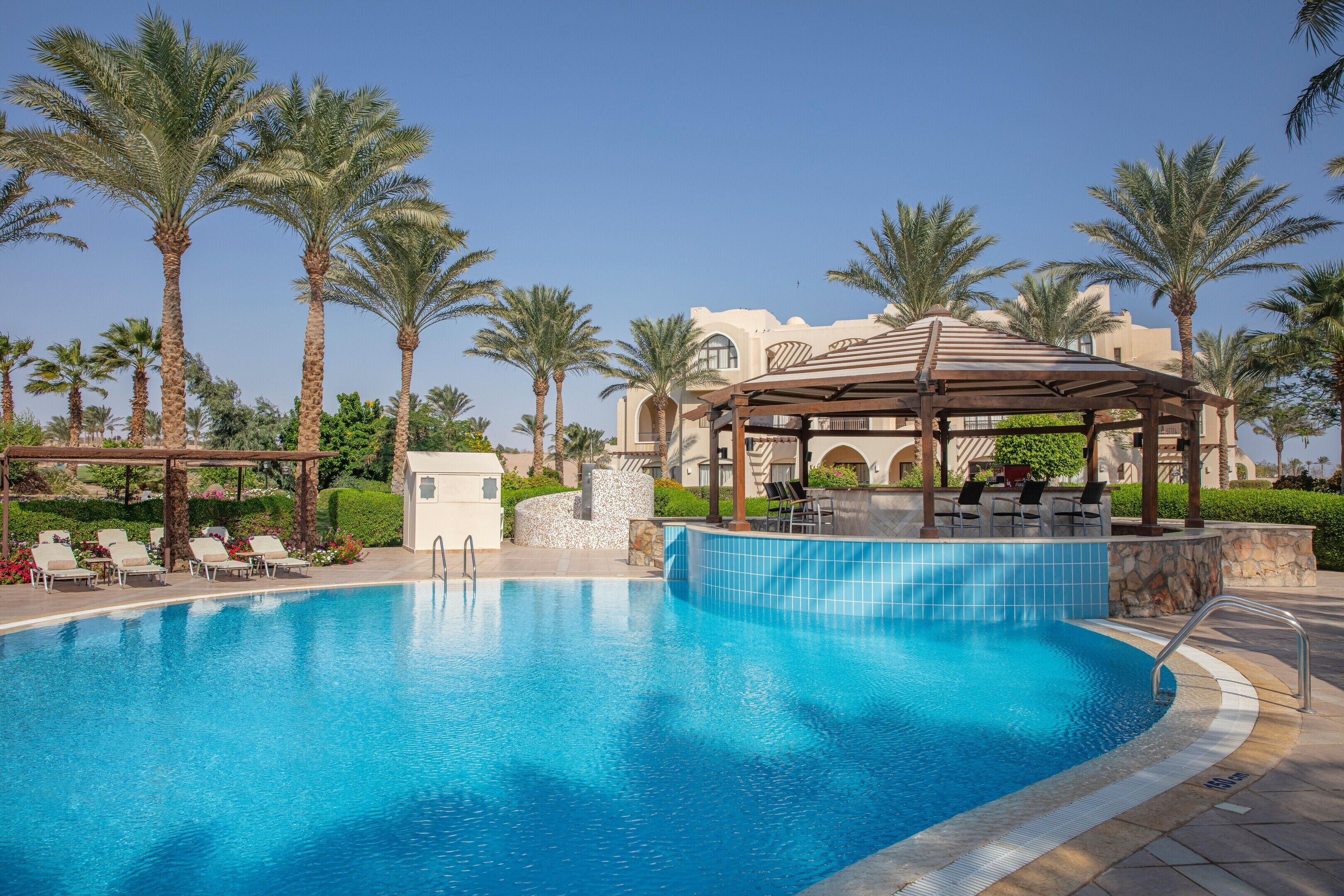 A swimming pool with lounge chairs, palm trees, and a gazebo.
