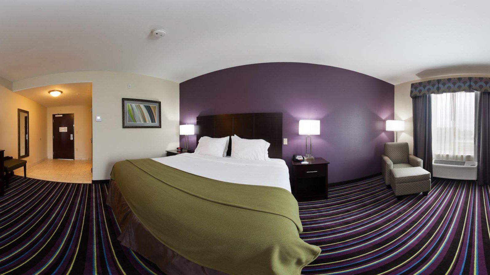 A hotel room with a large bed, a chair, a desk, and a window with curtains.