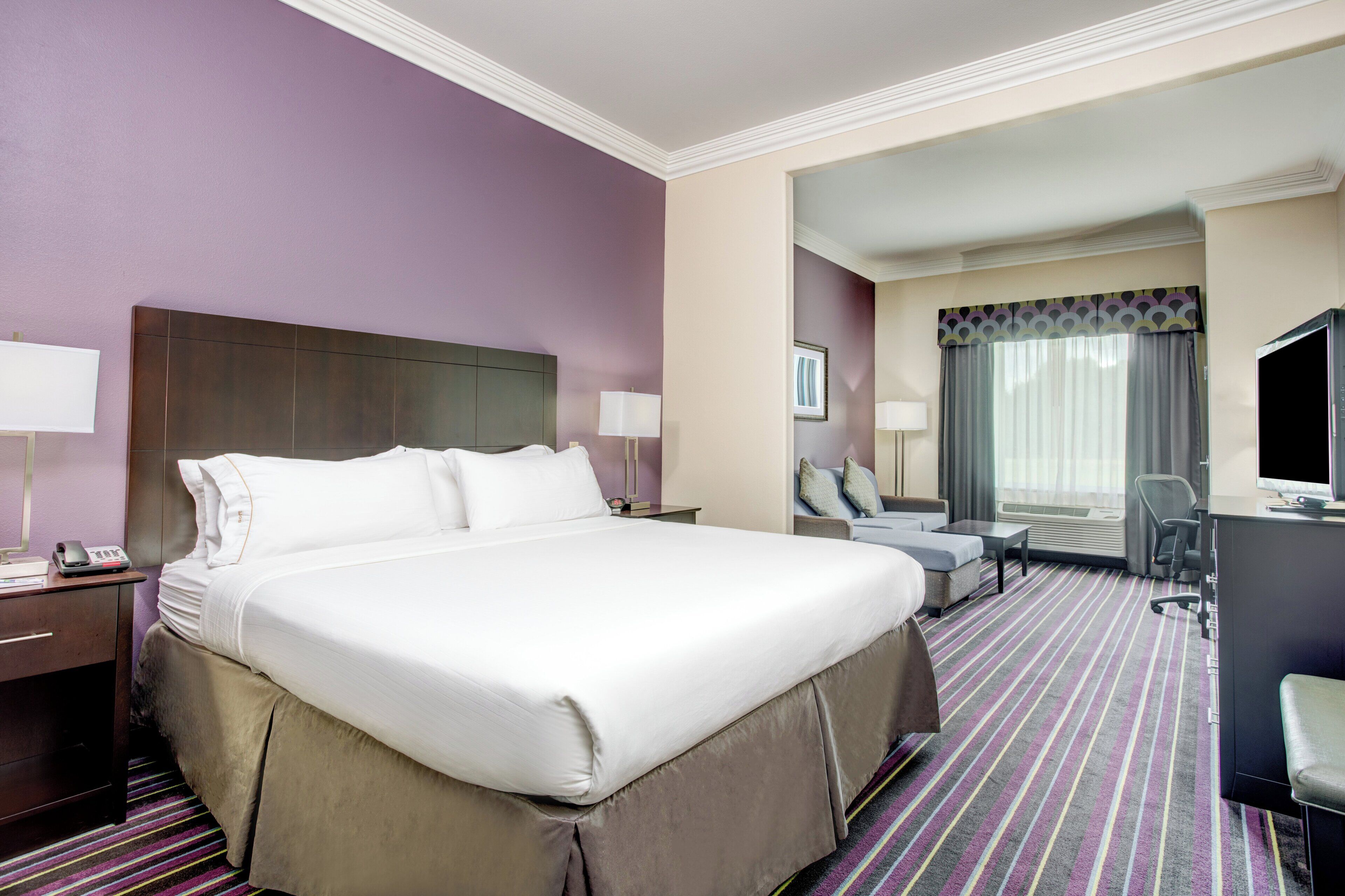 A hotel room with a large bed, a desk, a chair, and a television.