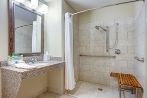 A bathroom with a granite countertop, a sink, a mirror, a shower with a grab bar, and a wooden bench. - Holiday Inn Express Hotel & Suites Raceland - Highway 90 by IHG (Raceland)