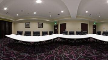 A conference room with a long table, multiple chairs, and framed pictures on the walls.