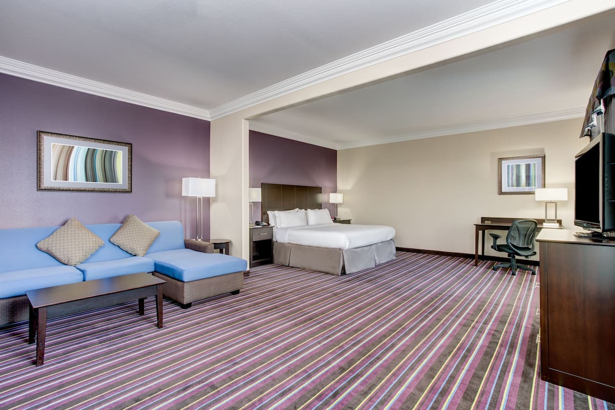 A hotel room with a blue sofa, a bed with white linens, a desk with a computer, and a TV.