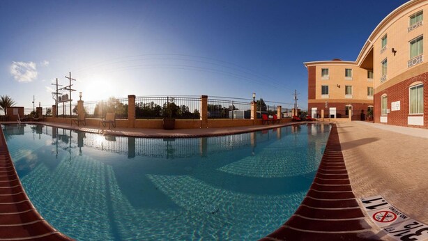 A swimming pool with a clear blue water surface, surrounded by a brick wall and a fence.