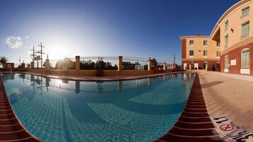 A swimming pool with a clear blue water surface, surrounded by a brick wall and a fence.