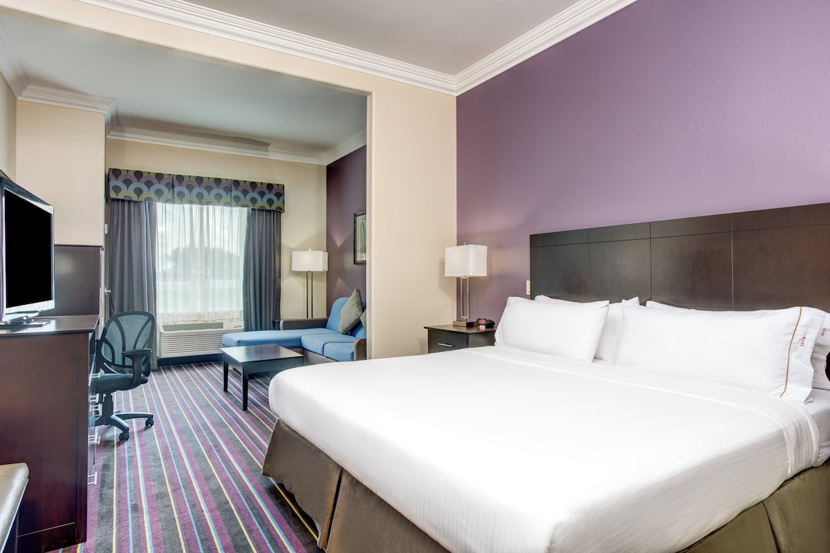 A hotel room with a large bed, a desk with a computer, a chair, and a sofa.