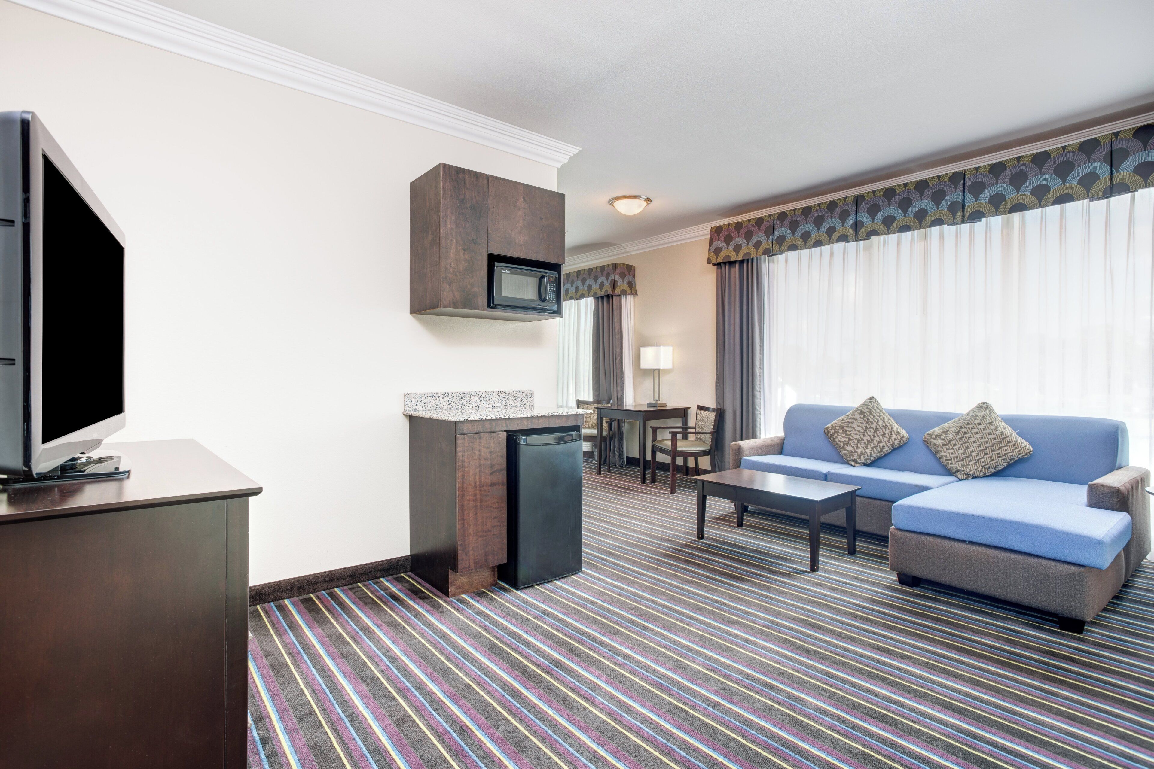 A hotel room with a television, a microwave, a sofa, a coffee table, and a striped carpet.