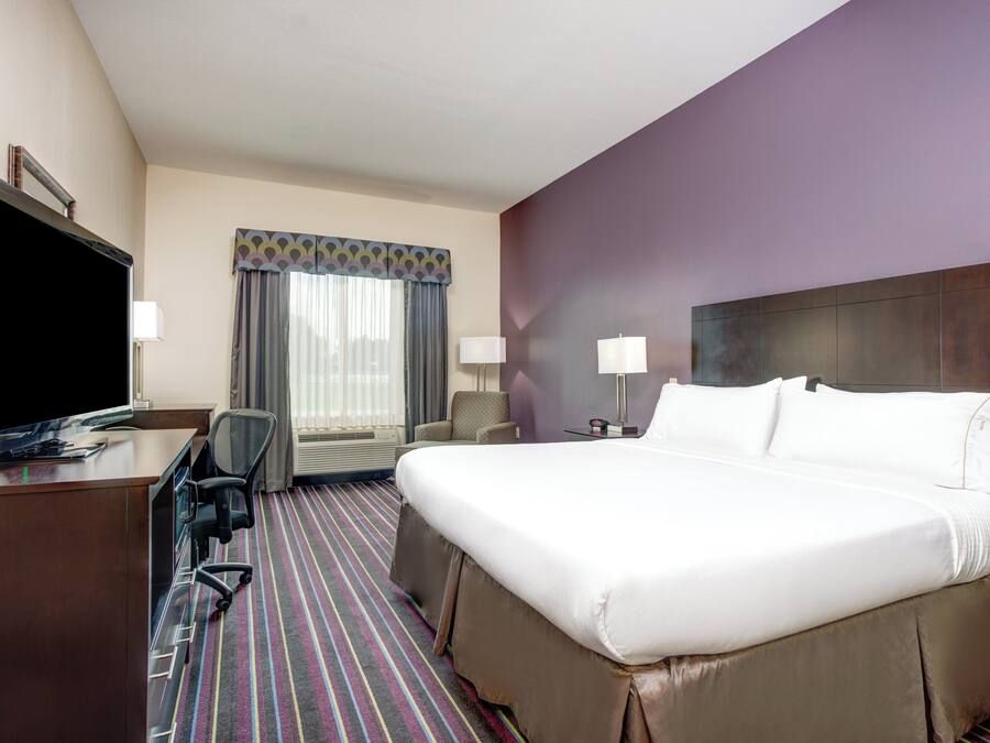 Habitación de hotel con cama, escritorio, televisión y ventana con cortinas.