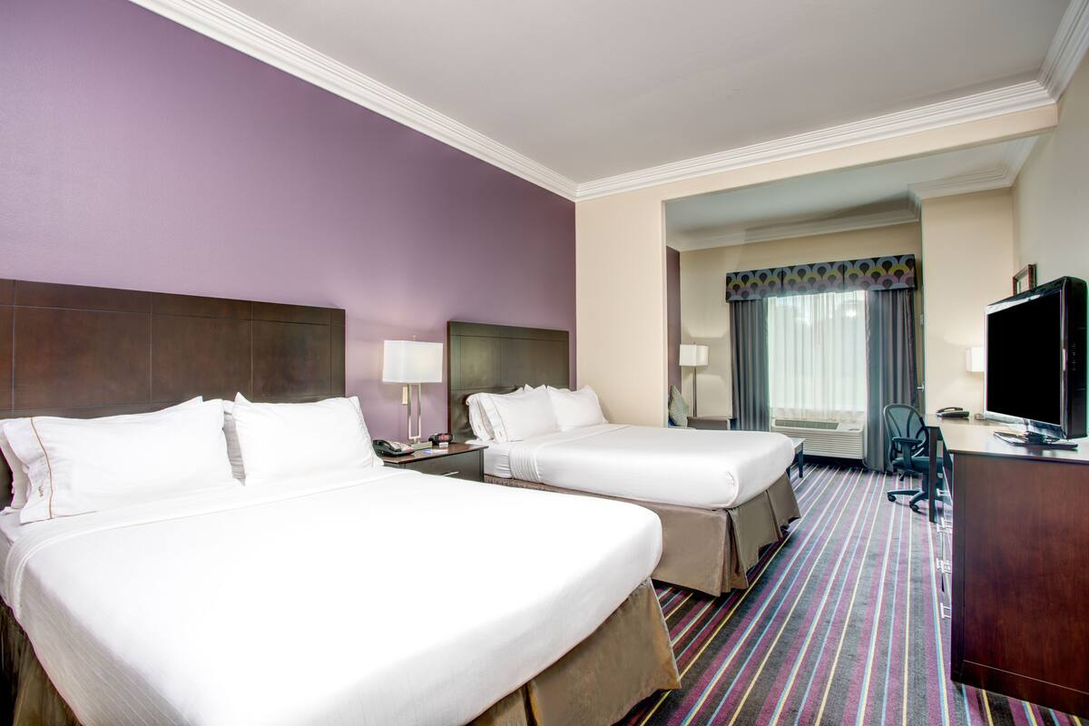 A hotel room with two beds, a desk, a television, and a window with curtains.