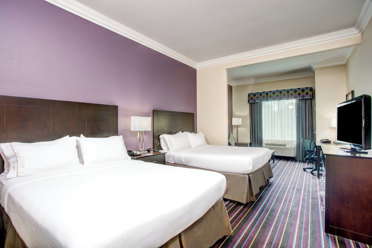 A hotel room with two beds, a desk, a television, and a bathroom visible through an open door.