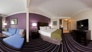 A hotel room with a bed, a sofa, a TV, a desk, and a lamp.