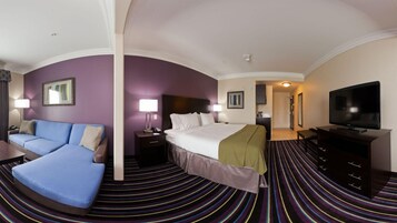 A hotel room with a bed, a sofa, a TV, a desk, and a lamp.