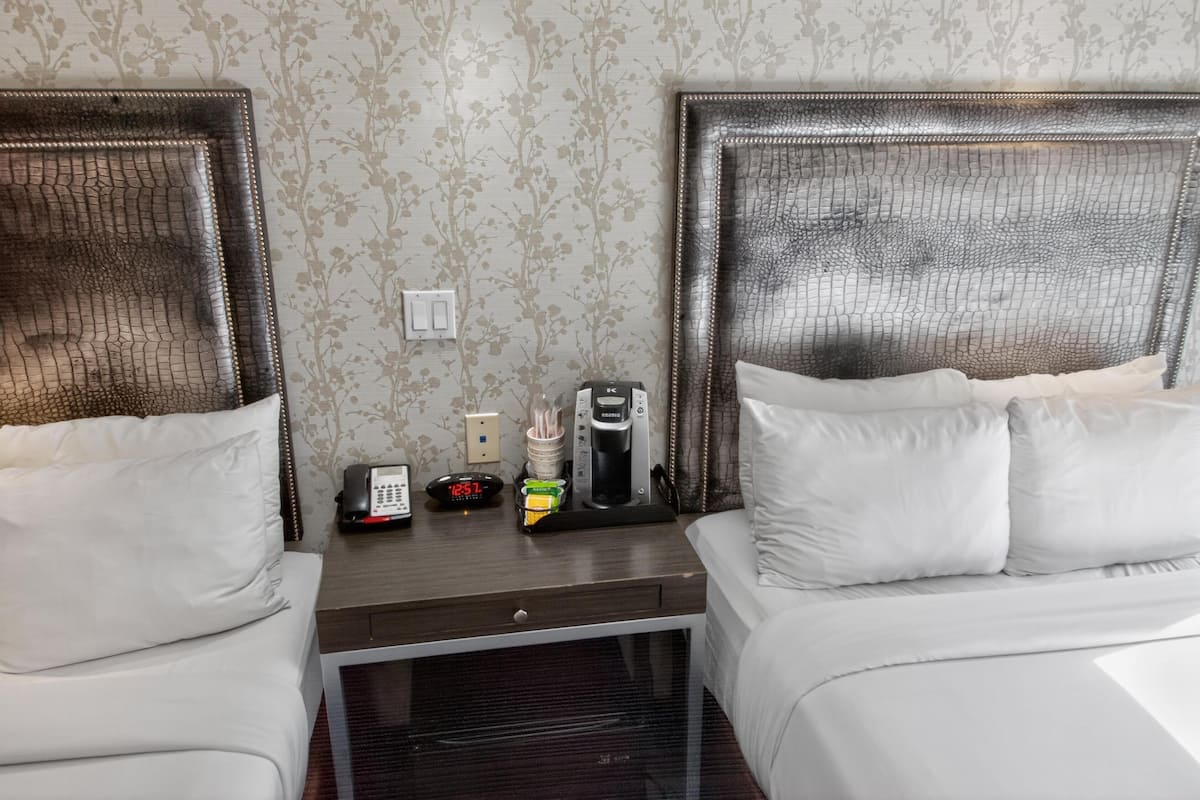 A hotel room with two beds, a nightstand with a phone, a coffee maker, and a clock.