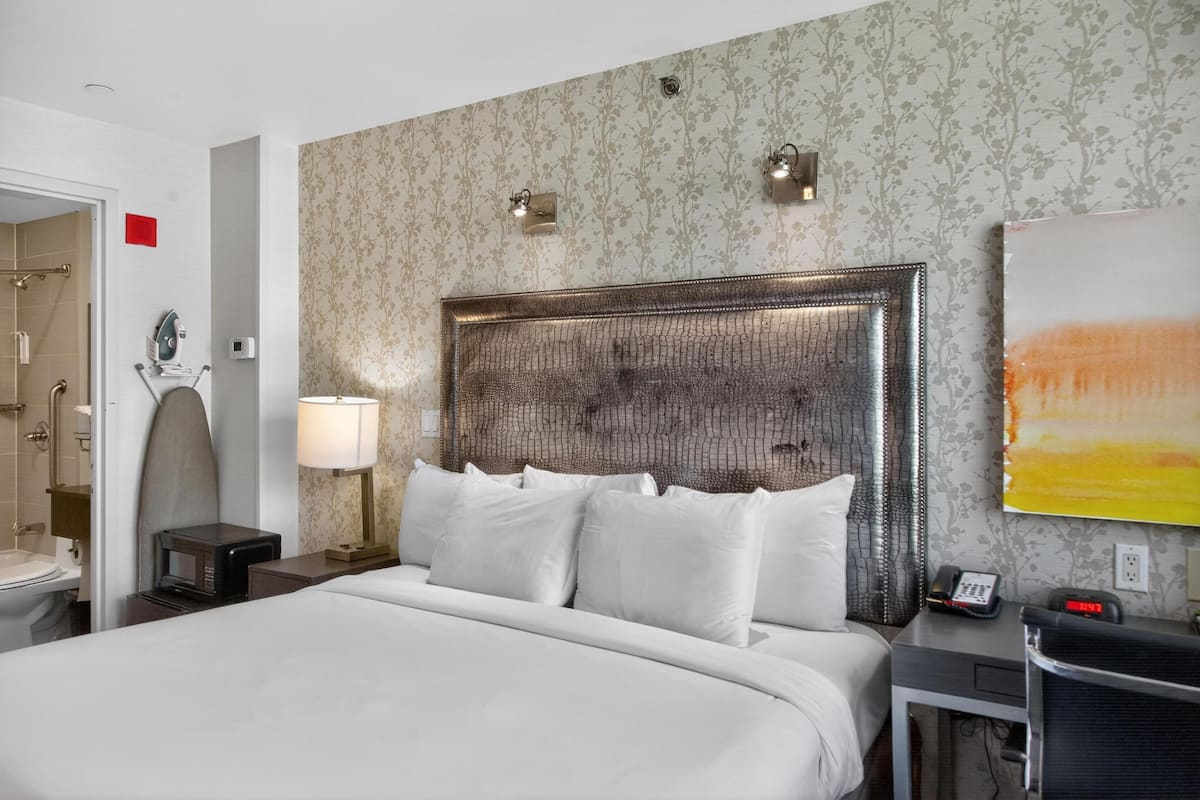 A hotel room with a large bed, a nightstand with a lamp, a telephone, and a wall-mounted light fixture.