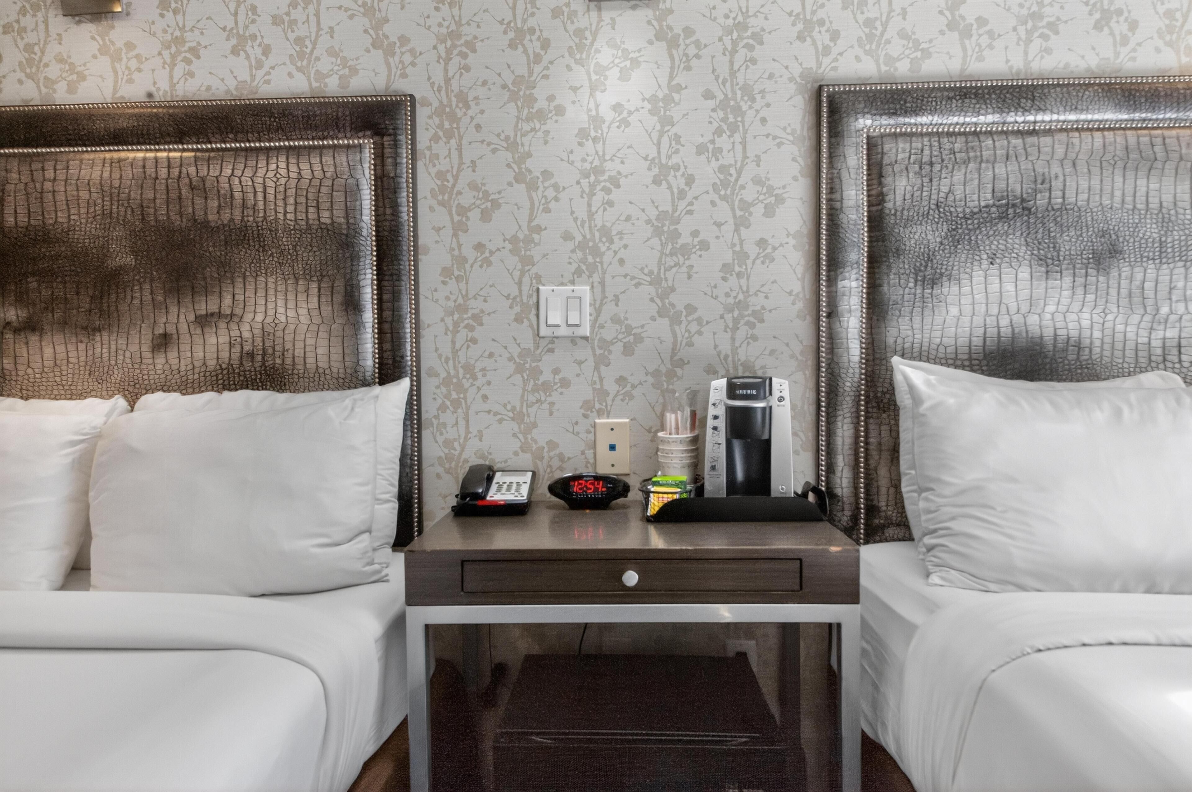 Habitación de hotel con dos camas, una mesita de noche, un reloj, un teléfono y una cafetera.