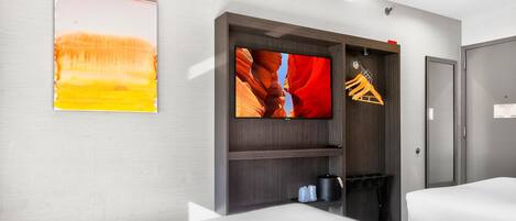 Una habitación de hotel con cama, televisor en la pared y perchero.