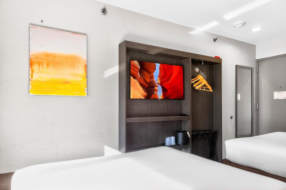 A hotel room with a bed, a TV mounted on a wall, and a coat rack.