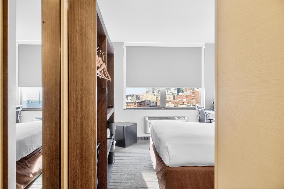 A hotel room with a bed, a desk, a chair, a wardrobe, and a view of the cityscape.