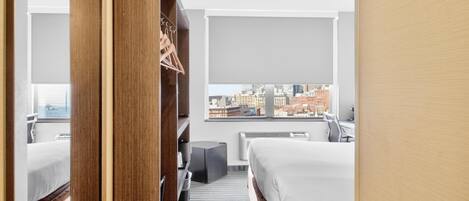 A hotel room with a bed, a desk, a chair, a wardrobe, and a view of the cityscape.