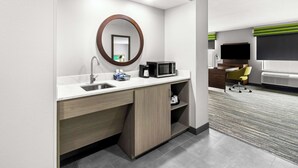 A modern hotel room with a kitchenette, a large mirror, a flat-screen TV, and a yellow chair. - Hampton Inn by Hilton Dayton South (Dayton)