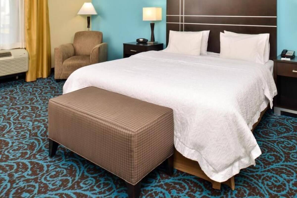 A hotel room with a large bed, a chair, a nightstand, and a patterned carpet.