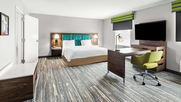 A hotel room with a bed, desk, chair, TV, and a door. - Hampton Inn by Hilton Dayton South (Dayton)