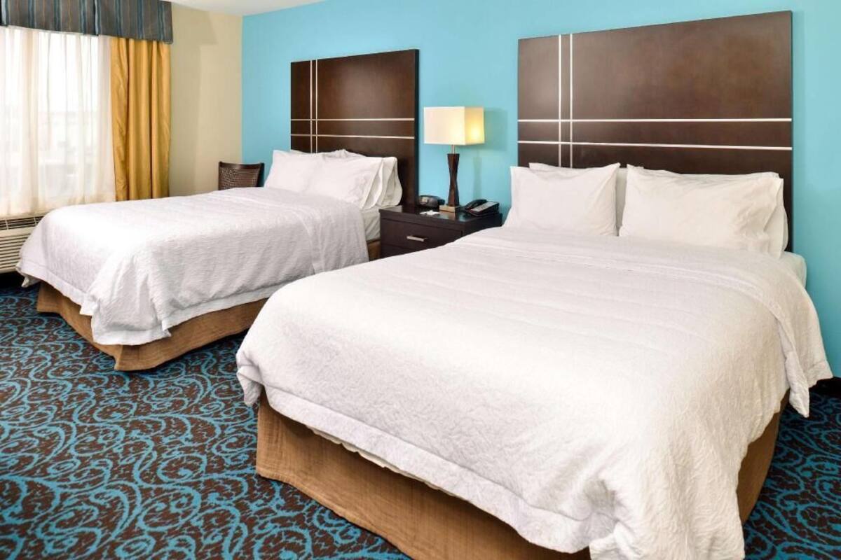 A hotel room with two beds, a nightstand with a lamp, and a patterned carpet.