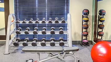 Un gimnasio con filas de mancuernas, una banca y pelotas de ejercicio.