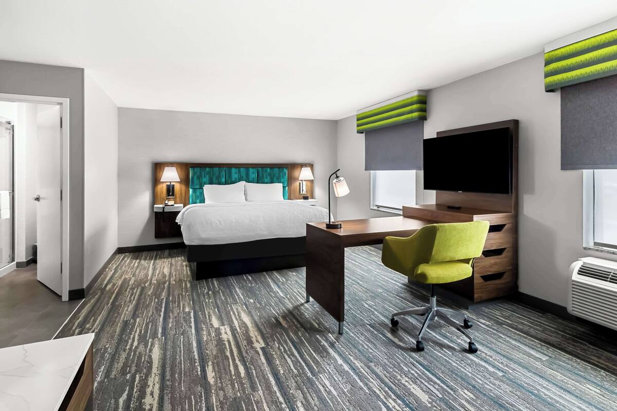 A hotel room with a bed, desk, chair, TV, and a large window.
