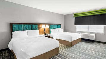 Habitación de hotel con dos camas, una mesita de noche con lámparas, una ventana con persiana oscura y un aire acondicionado instalado en la pared.