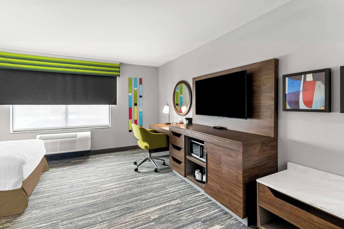 A modern hotel room with a bed, desk, and TV.