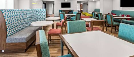 A modern hotel lobby with seating areas, tables, and a television.