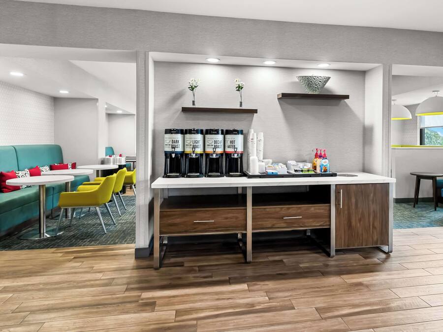 Quarto de hotel moderno com cozinha compacta, sofá, cadeiras amarelas e janela com vista.