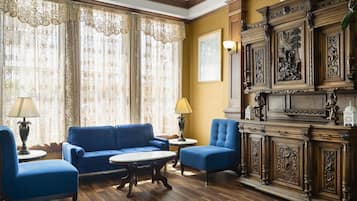 A room with a blue sofa, two armchairs, a wooden cabinet with carvings, and a large window with lace curtains.